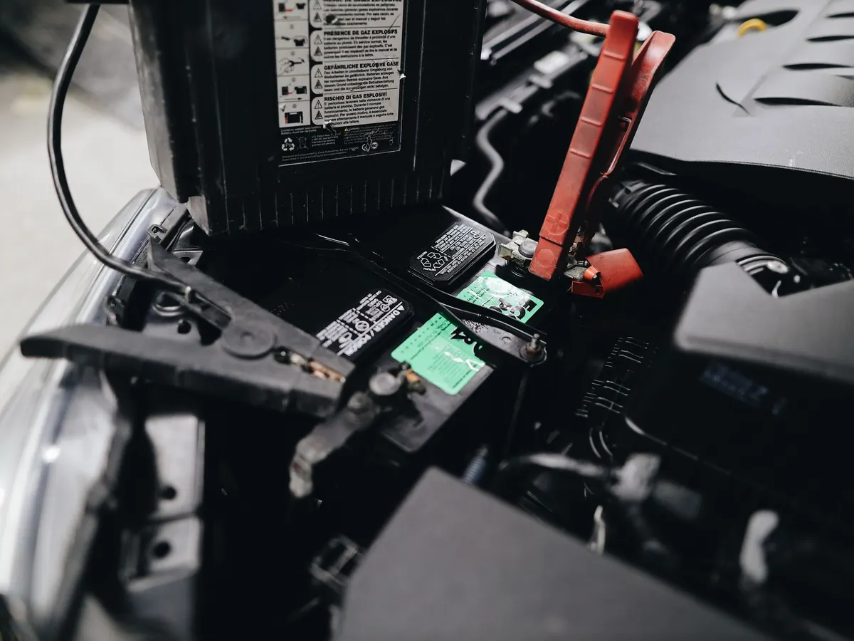 A car battery under the hood with jumper cables clamped to the terminals