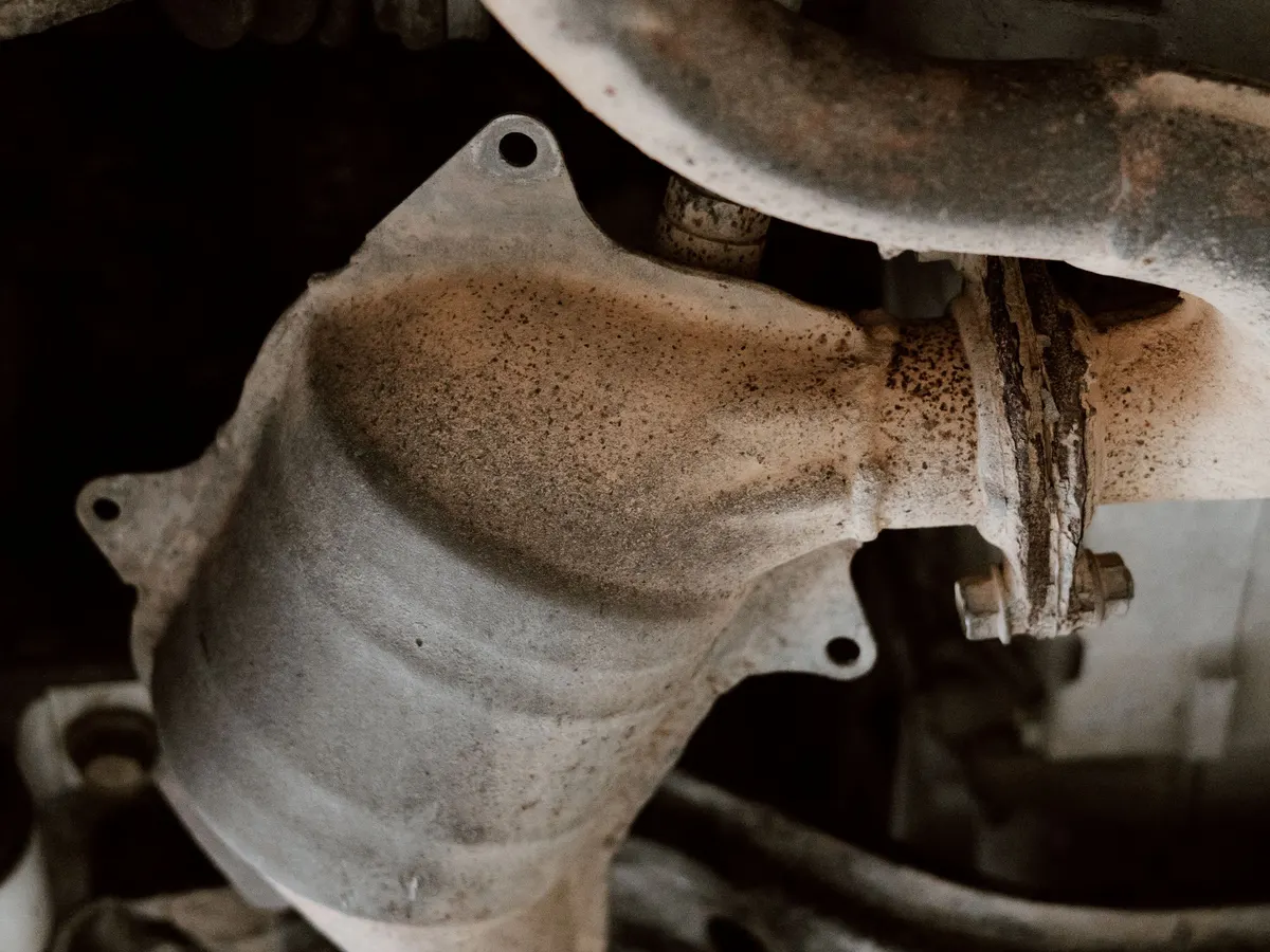 A close-up of an exhaust manifold and heat shield seen from underneath a vehicle