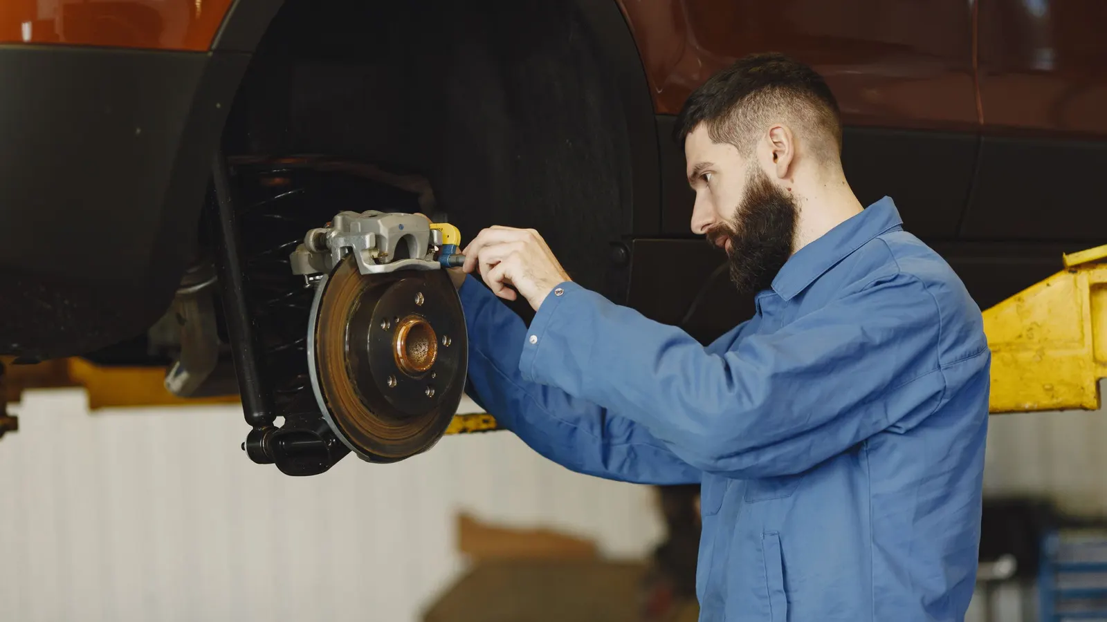 A technician working under the hood of a car in a bright, tidy workshop