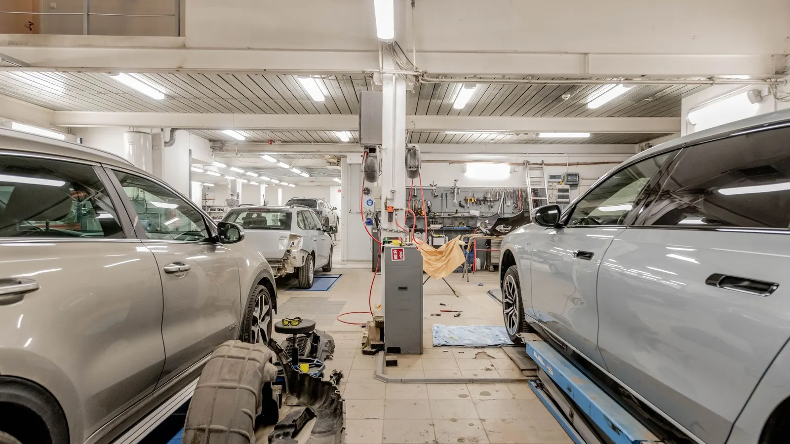 Two vehicles parked in service bays inside a bright, well-lit repair shop with tools hanging on the back wall
