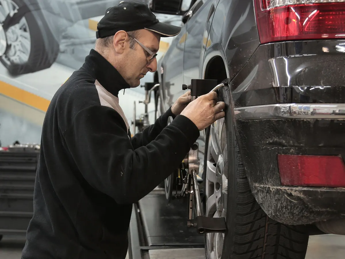 A technician in a black cap fitting an alignment sensor to a vehicle's front wheel