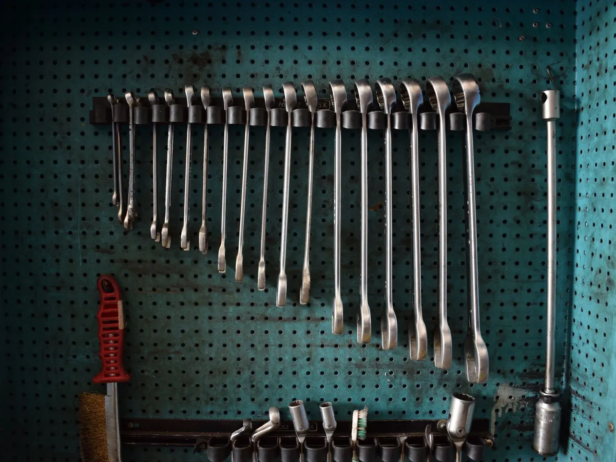 A pegboard wall with a row of combination wrenches hung in size order beside a few sockets and a wire brush