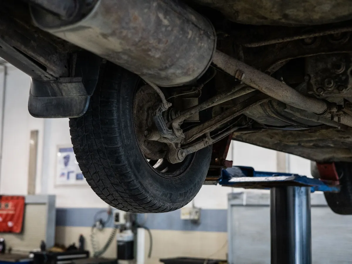 The underside of a vehicle raised on a lift, showing the exhaust, suspension arms and a rear wheel